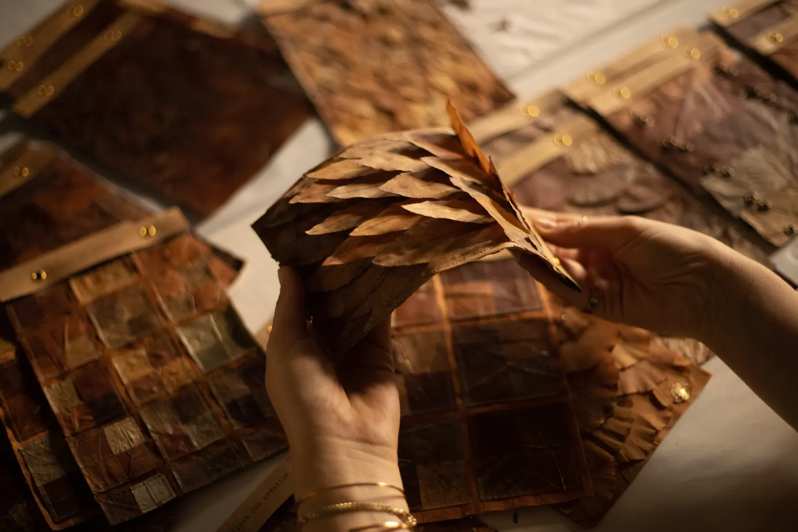 Mains d’Alyssa Jos travaillant une pièce en feuilles, échantillons sur la table